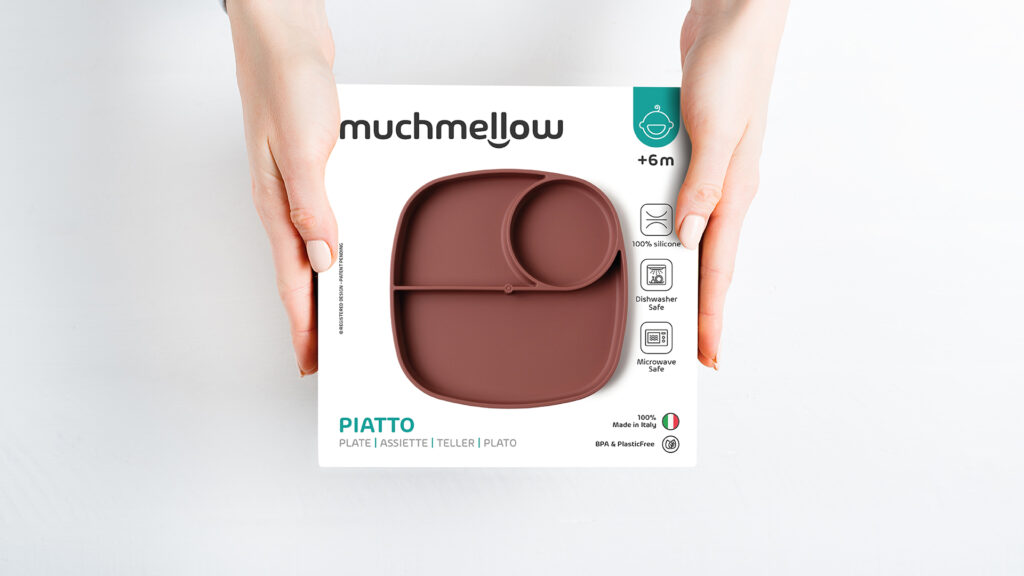Confezione del piatto in silicone Muchmellow fotografata tra le mani, con focus su materiali sicuri, lavabili e 100% made in Italy. Progetto di packaging design e shooting a cura di Meloria.
